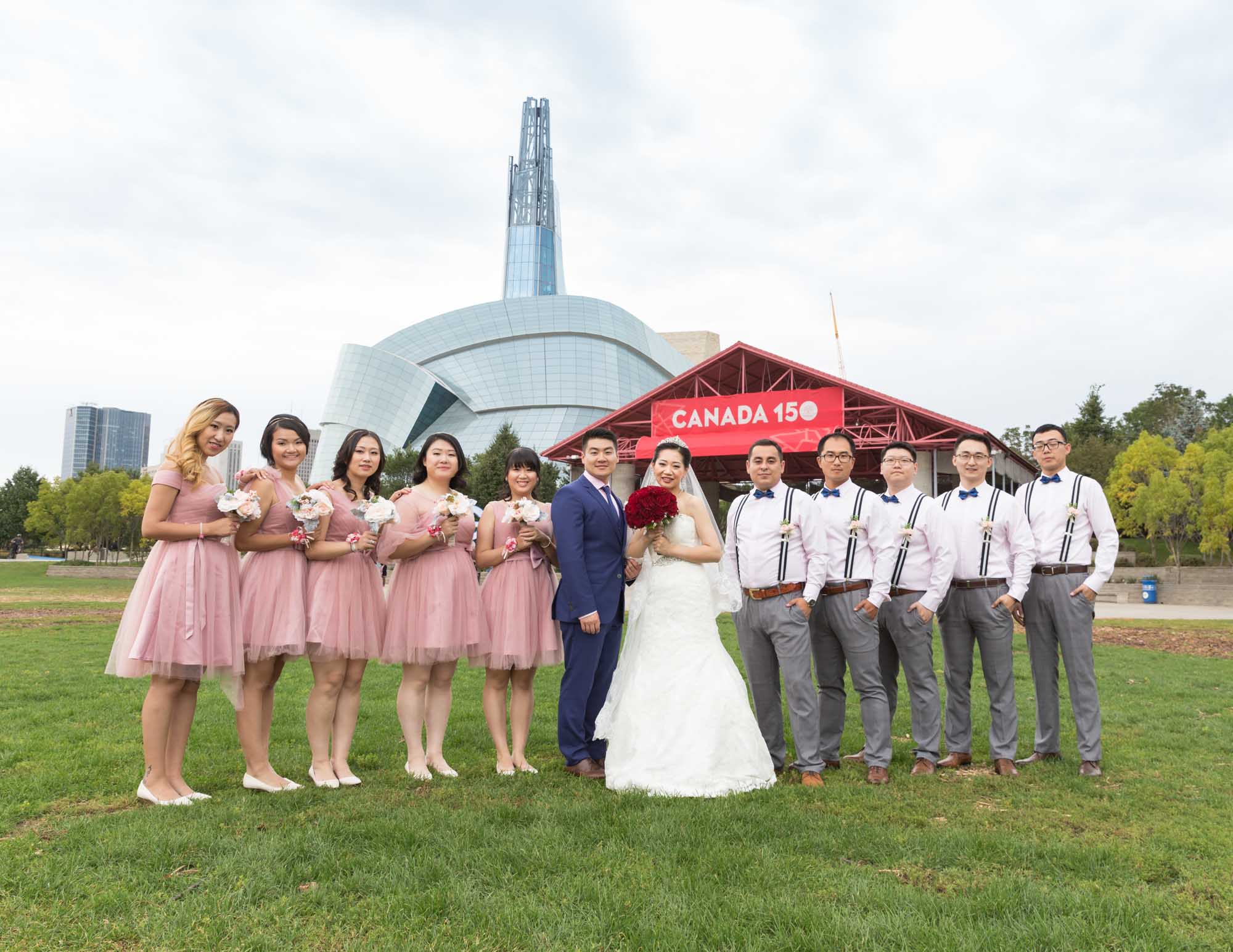 Image description: Wedding group photo of 12 people. with 5 groomsmen, 5 bridesmaids and the bride and groom in front of the Human Rights Museum in Winnipeg. Text reads: CANADA 150