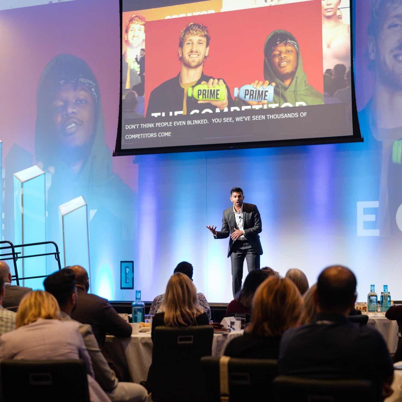 Image description: Keynote speaker in a dark gray suit and white shirt, giving a passionate speech.