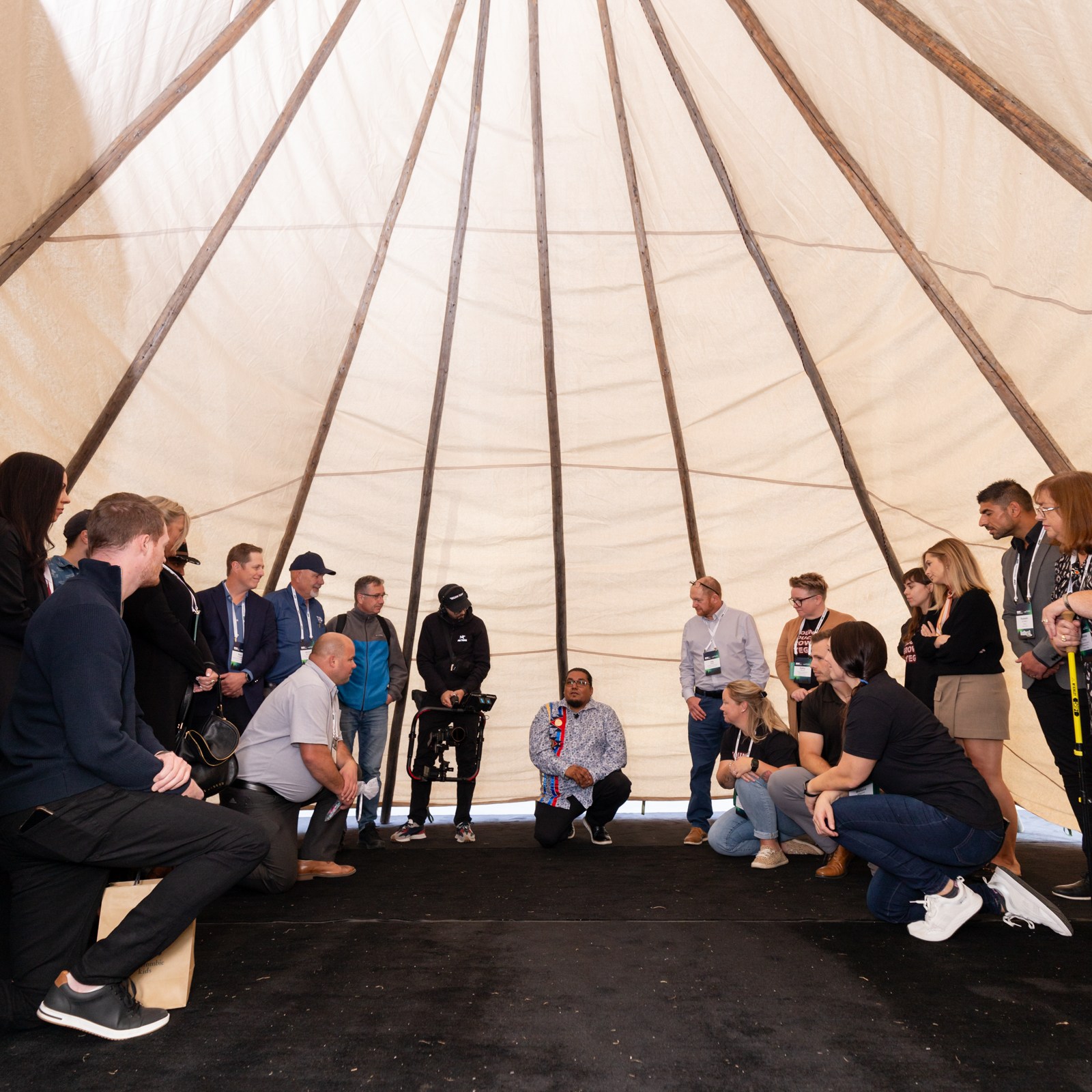 Image description: Under the tent, participants listened to the speaker explain the history of Tipi Raising