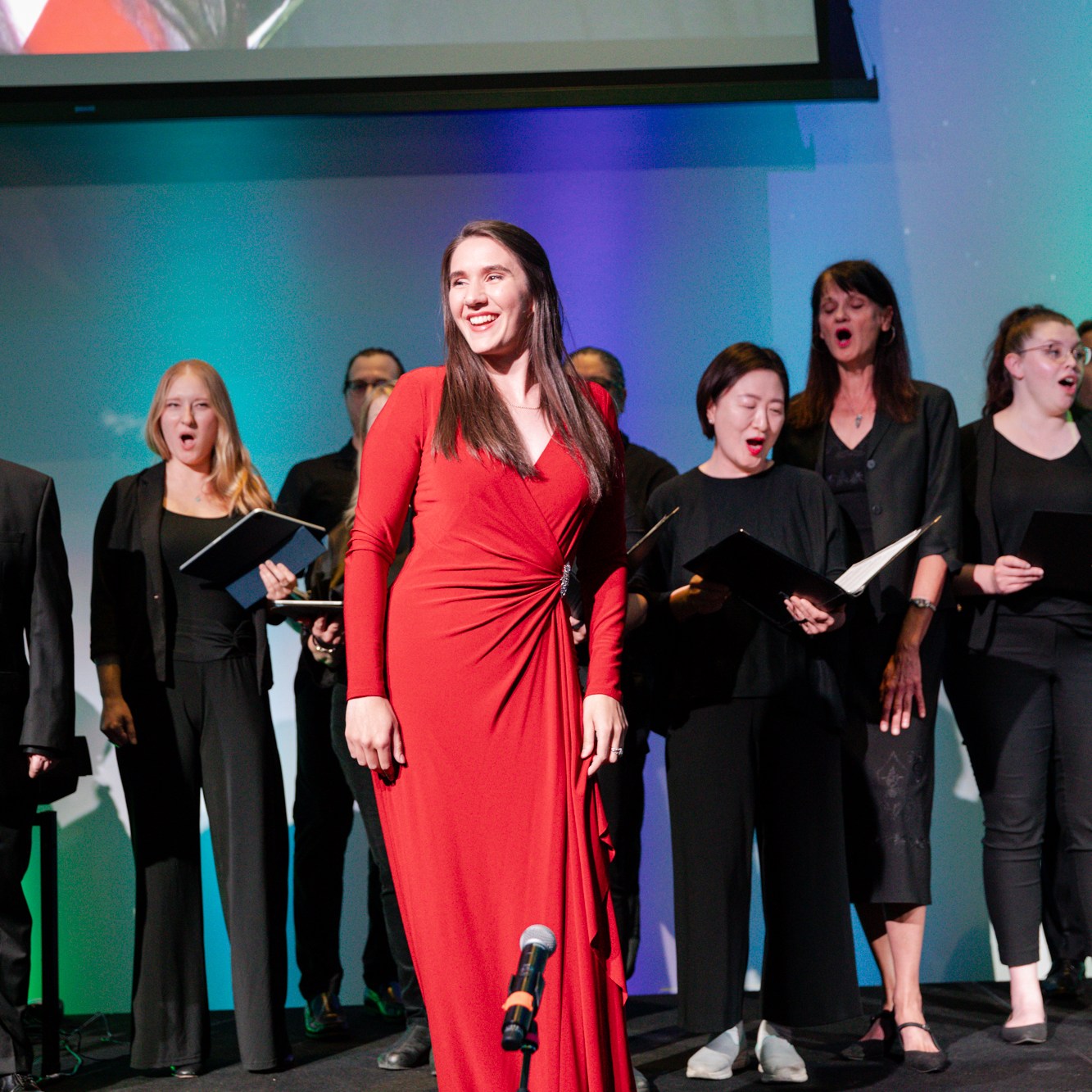 Image description: A female performer in a long red dress was singing, while others in black suits sang in the back