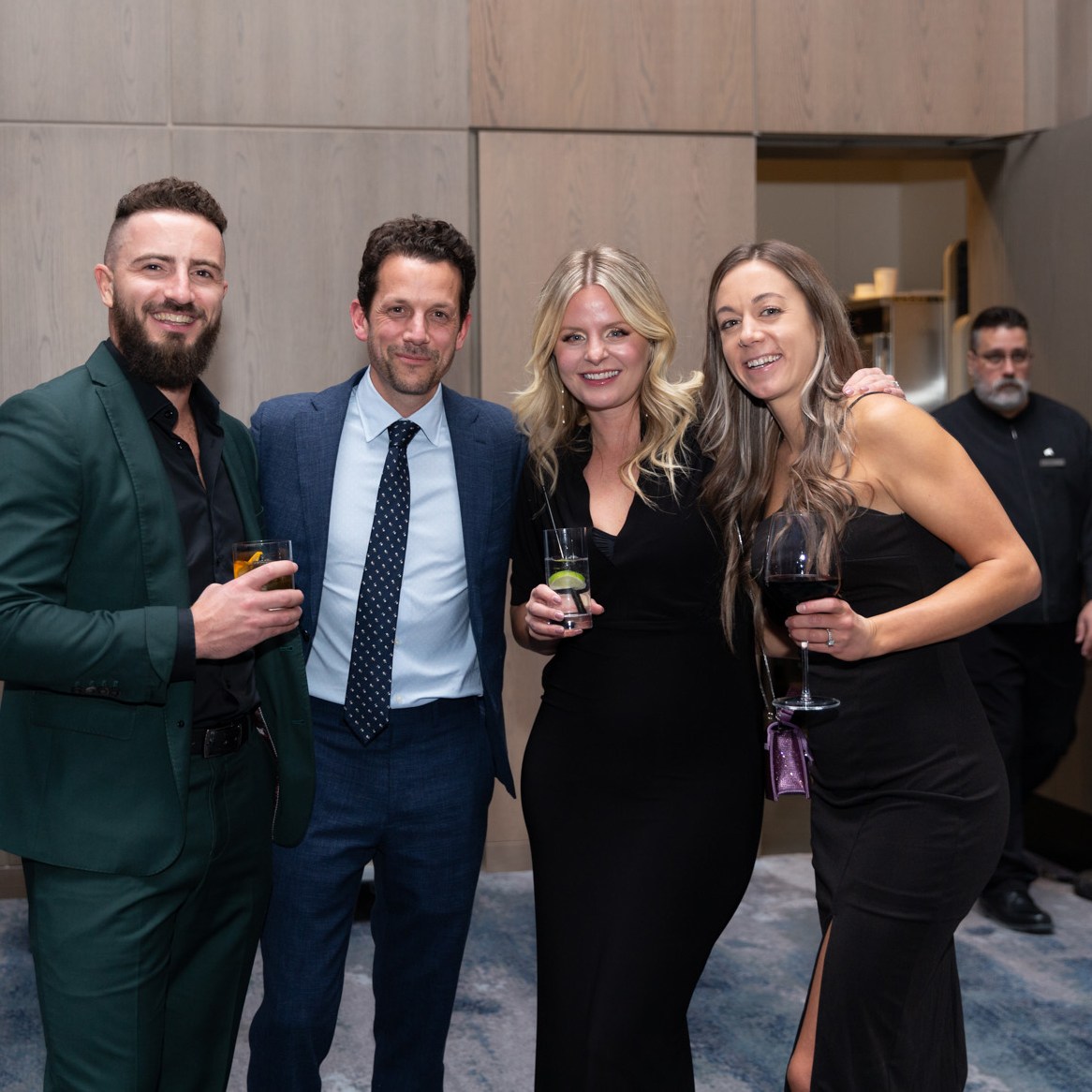 Image description: Two men and two women holding their respective wine glasses at the year-end party.