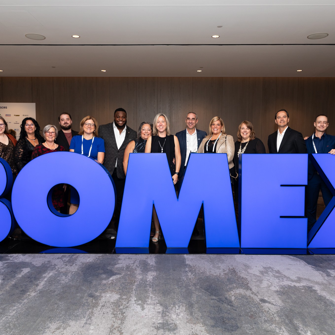 Image description: A group photo of a group of participants behind a large blue BOMEX logo. Text reads: BOMEX