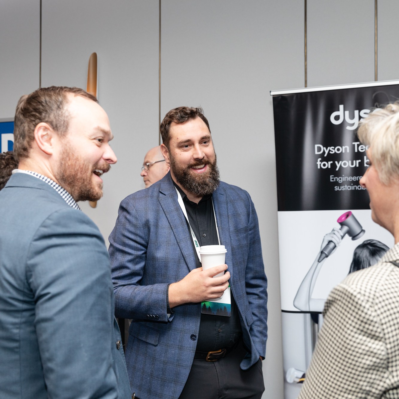 Image description: The sponsors are talking. Two men and a woman in front of a billboard. Text reads: ON SIDE, Dyson