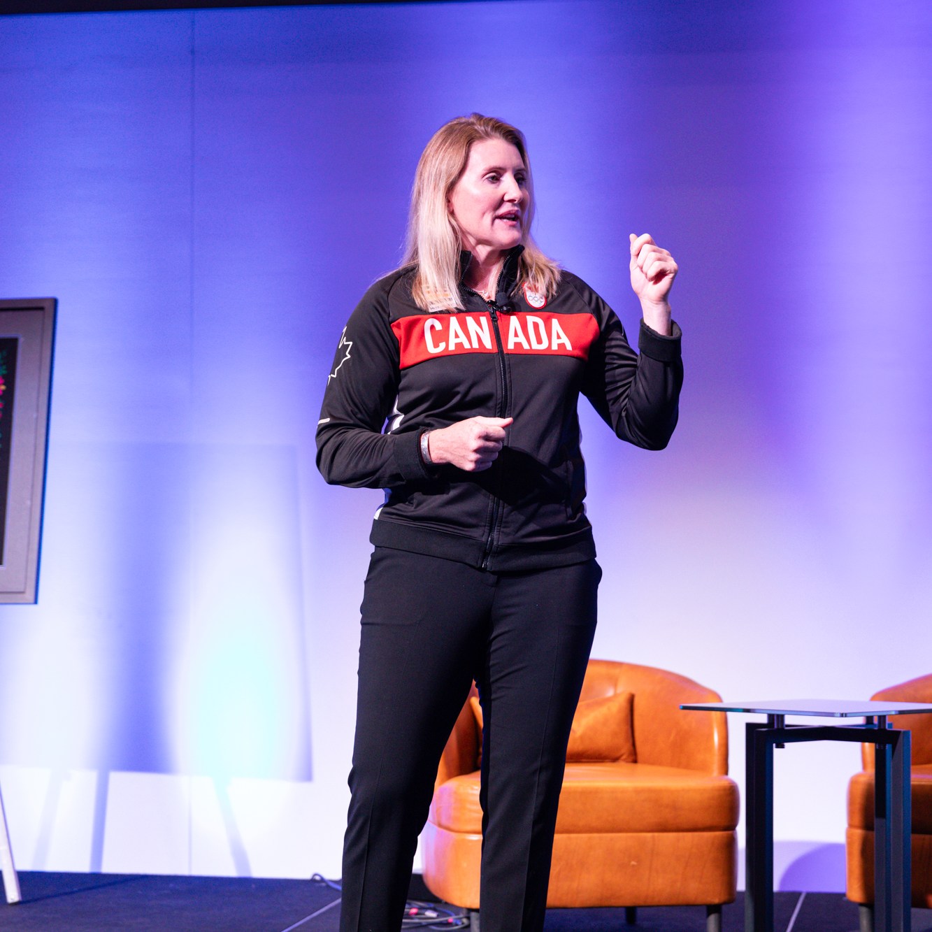 Image description: A female Keynote presented on stage, in front of a purple background. Text reads: CANADA