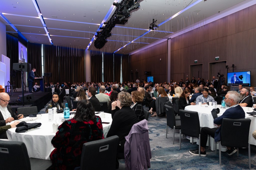 Image description: An image of a corporate event for 500 people, the host was speaking, and the attendees listened attentively around the white table and applauded him.